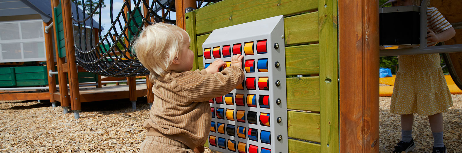 A young toddler plays with a play panel at a playground, it's a sorting game.